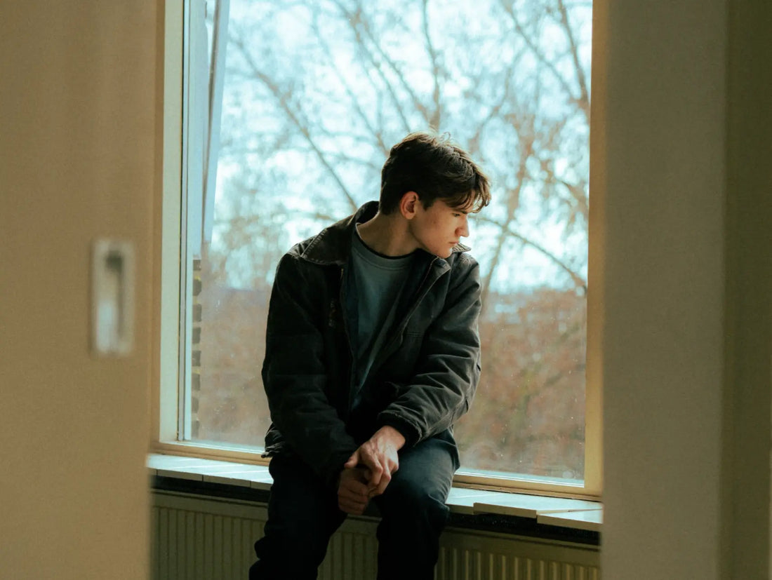 Person looking out a window in quiet reflection, representing mental wellness in a Medicine Box blog