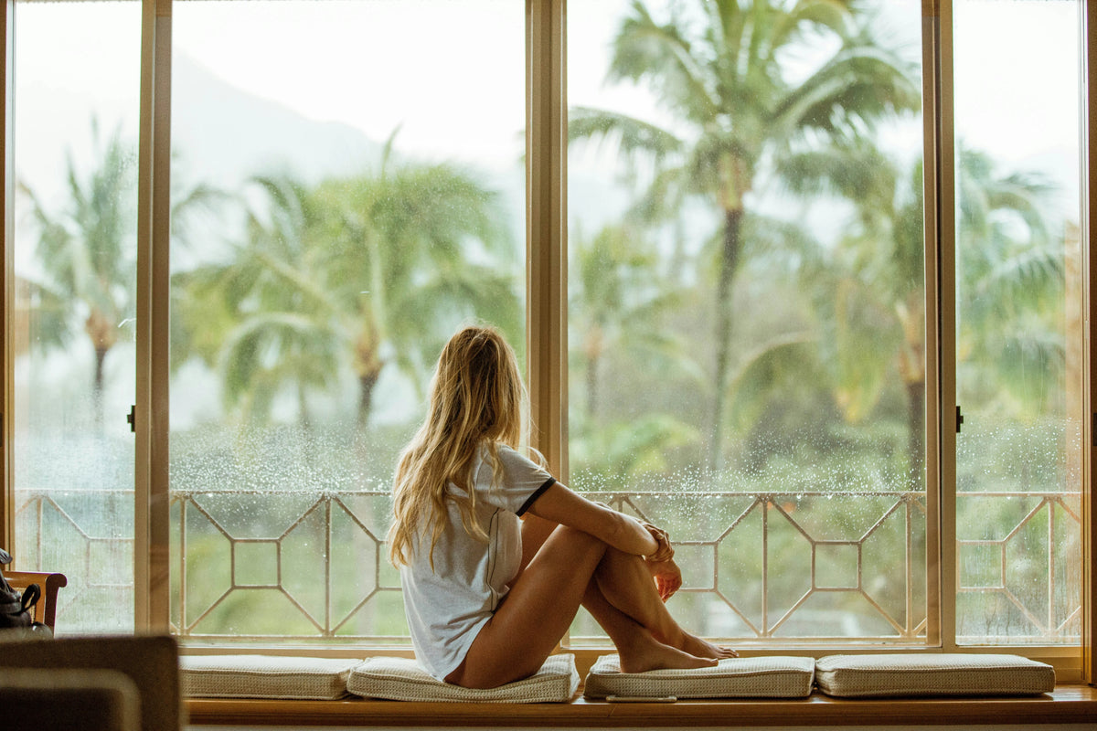 Woman sitting by a large window with palm trees outside in a medicine box blog